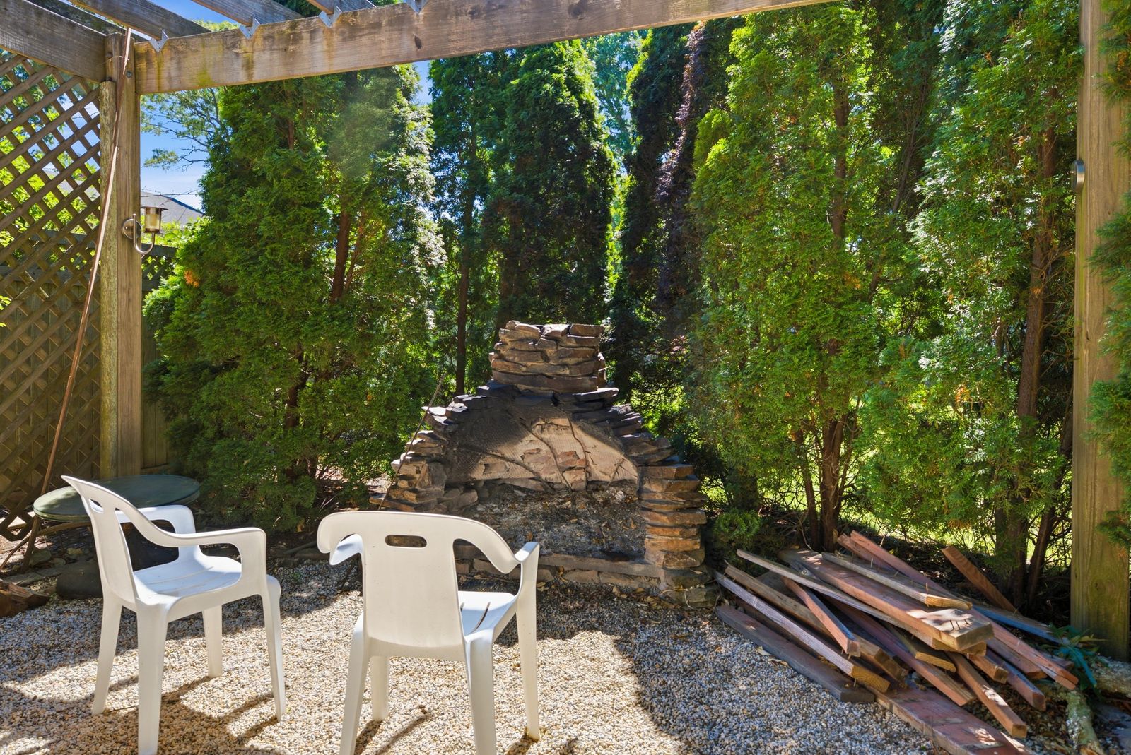 Stone outdoor fireplace under a pergola surrounded by evergreens in Cape May Court House NJ