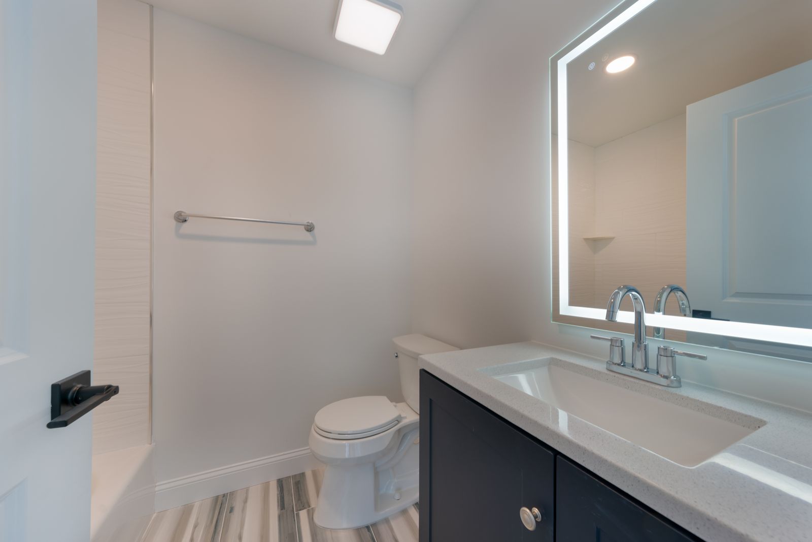 Bathroom with backlit mirror and dark vanity