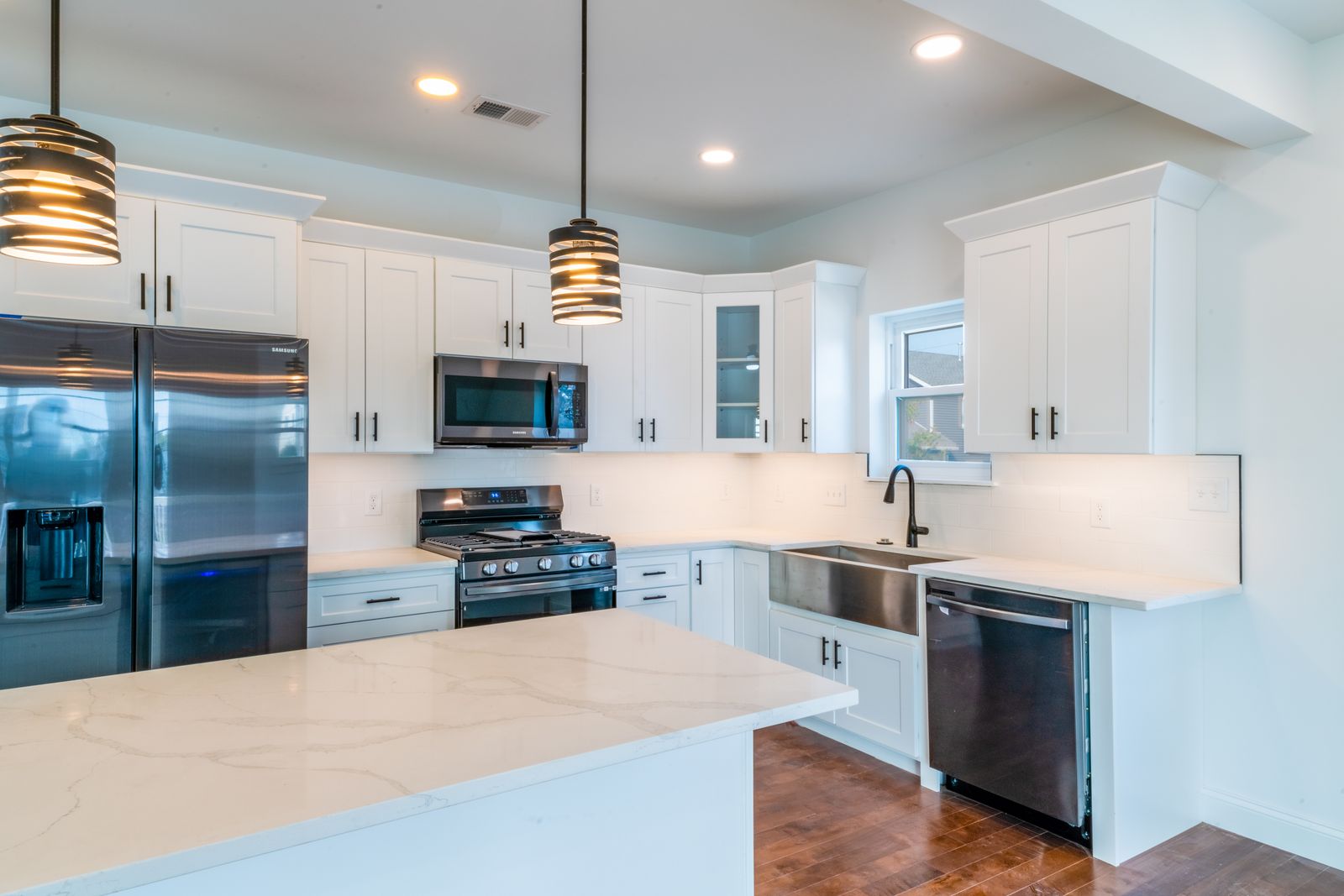 White kitchen with quartz island, pendant lights and stainless appliances